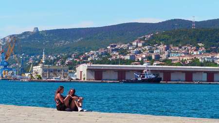 TRIESTE, ITALY - AUGUST 11, 2017. Young women chatting on the pier against seaport and cityのeditorial素材