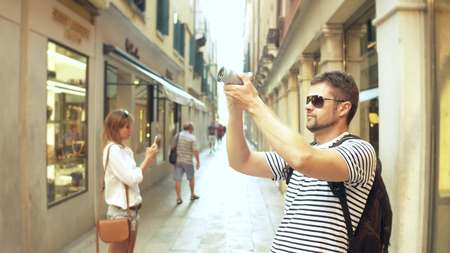 Young handsome bearded man making photos of a narrow street with his camera