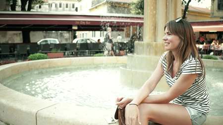 Beautiful young woman sitting near the street fountainの写真素材