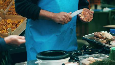 Male vendor shelling scallops at local seafood stall on the marketplace