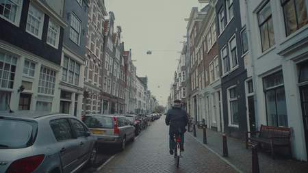 AMSTERDAM, NETHERLANDS - DECEMBER 26, 2017. Man cycling along typical street of the cityのeditorial素材