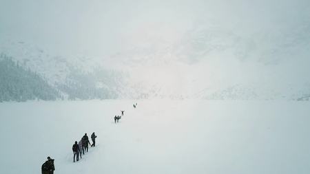 Aerial shot of unrecognizable people hiking on the frozen mountain lake Sea Eye in the snow, Polandの写真素材