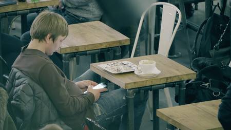 WARSAW, POLAND - MARCH 14, 2018. Young man using his smartphone in a cafe