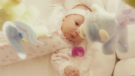 Baby girl looking at defocused toy mobile in her cot