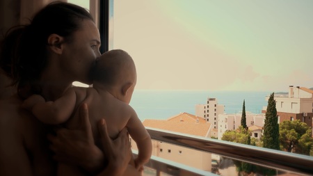 Mother and her little baby look at sea through the window on vacationの写真素材