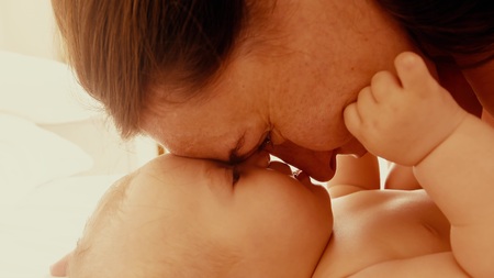 Mother playing with her little baby in sunny bedroomの写真素材