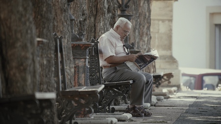 VALENCIA, SPAIN - SEPTEMBER 22, 2018. Elder man sitting on park bench and reading newspaperのeditorial素材