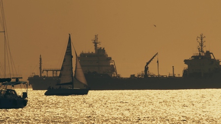 GIBRALTAR, GREAT BRITAIN - SEPTEMBER 27, 2018. Silhouette of maneuvering sailboat and distant cargo ships at sunsetのeditorial素材