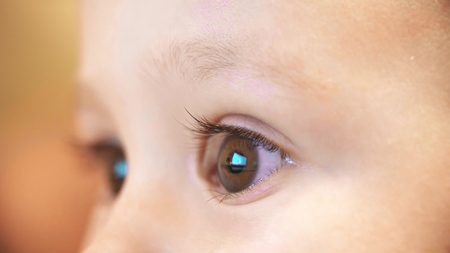 Unknown cartoon on computer screen reflects in babys eyes. Close-up shotの写真素材