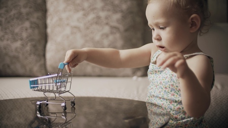 Funny baby girl plays with toy shopping cartの写真素材