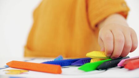 Blonde baby girl putting yellow crayon on the tableの写真素材
