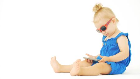 Focused baby girl wearing sunglasses watches movie or cartoon on a smartphone