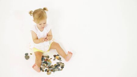 Blonde baby girl plays with sea pebble. Vacation related clipの写真素材
