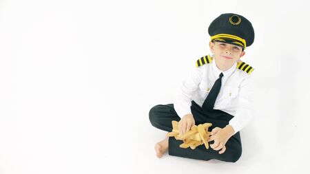 Boy wearing pilots uniform plays with generic wooden toy planeの写真素材