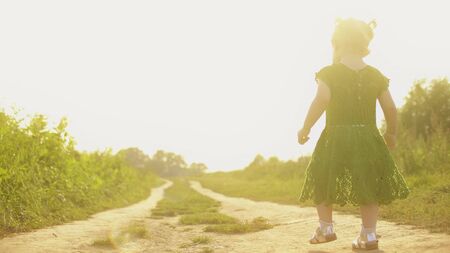 Baby girl walking along rural field pathway on a sunny summer eveningの写真素材