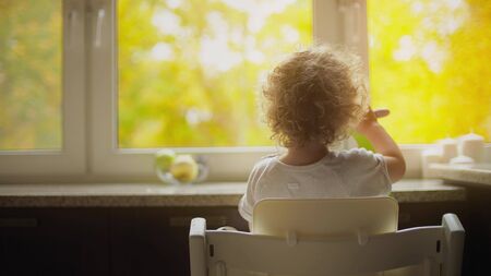 Blonde baby eats in front window facing beautiful autumn parkの写真素材