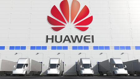 Modern semi-trailer trucks at warehouse loading bay with HUAWEI logo on the wall. Editorial 3D...