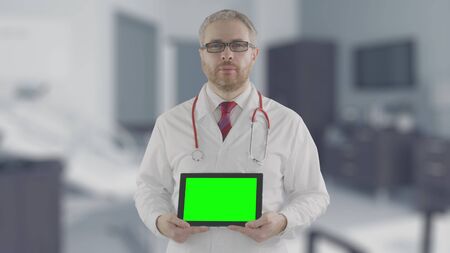 Concerned doctor holds modern tablet PC with green screenの写真素材