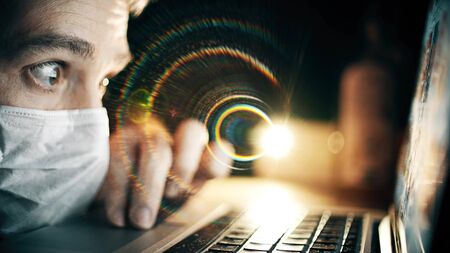 Terrified man wearing face mask browses medical news sites on his laptop. Latest COVID-19 outbreak data related clipの写真素材