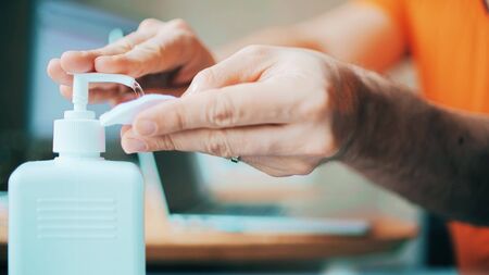 A man working from home uses disinfectant to clean his laptop. Workplace hygiene during COVID-19...