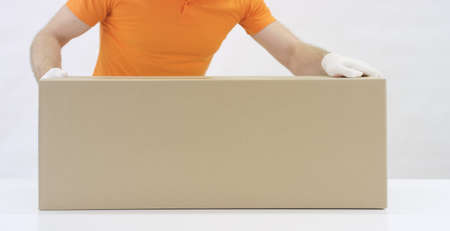 A warehouse worker in orange uniform pushes a big heavy carton on table