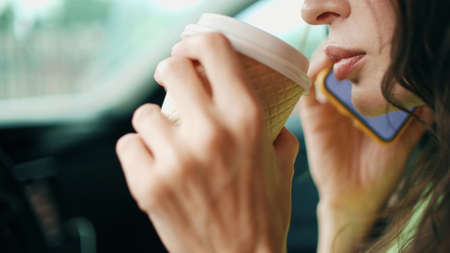 Beautiful young woman drinks coffee from disposable cup while talking on the phone in a car