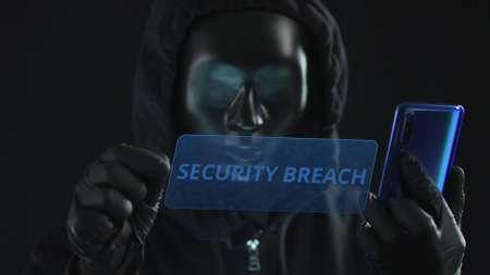 Hacker wearing black mask pulls SECURITY BREACH tab from a smartphone. Hacking conceptの写真素材