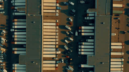 Aerial overhead shot of a big warehouse and many loading and unloading trailer trucks. Logistics conceptの写真素材