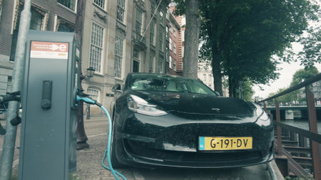 AMSTERDAM, NETHERLANDS - JULY 10, 2022. Charging electric Tesla car in the street