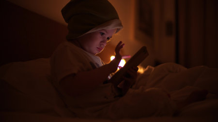 Funny focused baby girl uses smartphone in the bed. New user conceptの写真素材