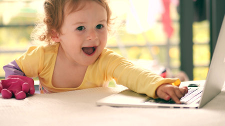 Funny little girl wearing rubber glove works on the laptop at home with a prankster smileの写真素材