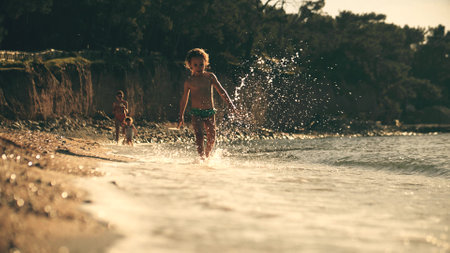 Little kid running in shallow water along the sea beach, slow motion. Summer vacation timeの写真素材