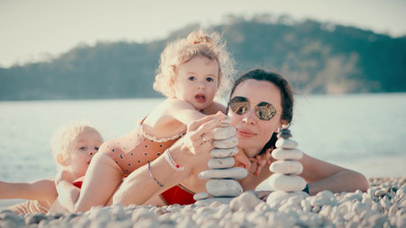 Mother and her two little girls having a good time on the beach. Building a pebble tower, faamily life balance conceptの写真素材