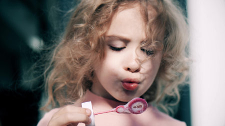 Beautiful little blonde girl in pink blows soap bubbles, close-upの写真素材