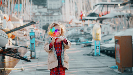 Happy blonde little girl holds toy rainbow windmill in marina