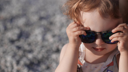 Funny little baby girl wears big sunglasses on the beachの写真素材