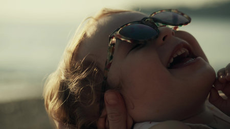 Mother holds smiling little baby girl wearing sunglasses, close-upの写真素材