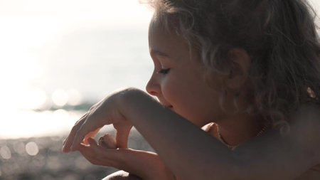 Happy blonde little girl plays with pebble on the beach, close-up portraitの写真素材