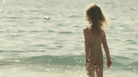 Little blonde girl plays with waves on the beach on a sunny summer dayの写真素材