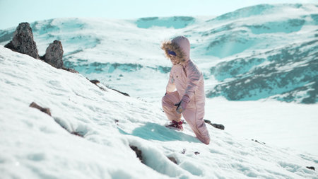 Beautiful little girl in pink snowsuit hiking in snow in scenic mountainsの写真素材