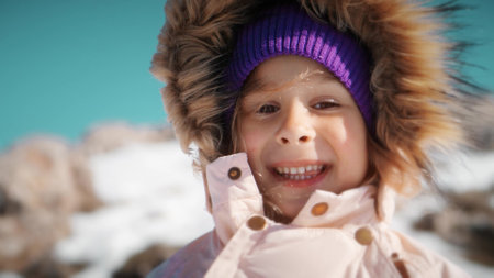 Close-up portrait of a beautiful little girl wearing warm clothes in snowy mountains in winter