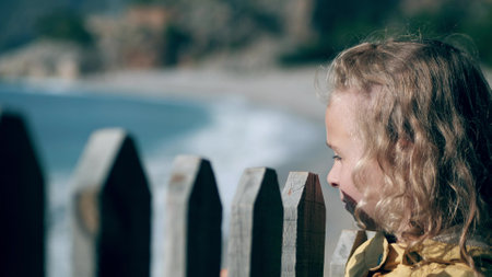 Sad little girl looks at sea behind the fence. Limitation or border conceptsの写真素材