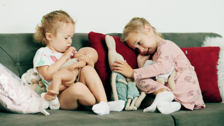 Little girls play with dolls on the sofa at homeの写真素材