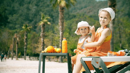 Cheerful little girls wearing orange clothes have picnic on the beachの写真素材