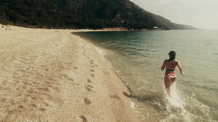 Aerial slow motion shot of a beautiful slim woman in striped swimsuit running on the beachの写真素材