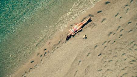 Aerial overhead shot of a beautiful slim woman in striped swimsuit laying on the beachの写真素材