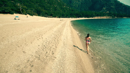 A Beautiful woman in striped swimsuit running on the beach, aerial drone slow motion shotの写真素材