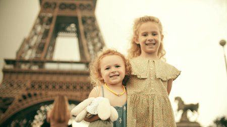 Two smiling little sisters hug each other and pose at the famous Eiffel Tower. Paris, Franceの写真素材