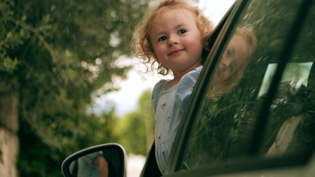 Cheerful little girl looks out of the driver side window of a parked carの写真素材