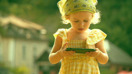 Cute little girl walks with with a smartphone on a sunny summer dayの写真素材